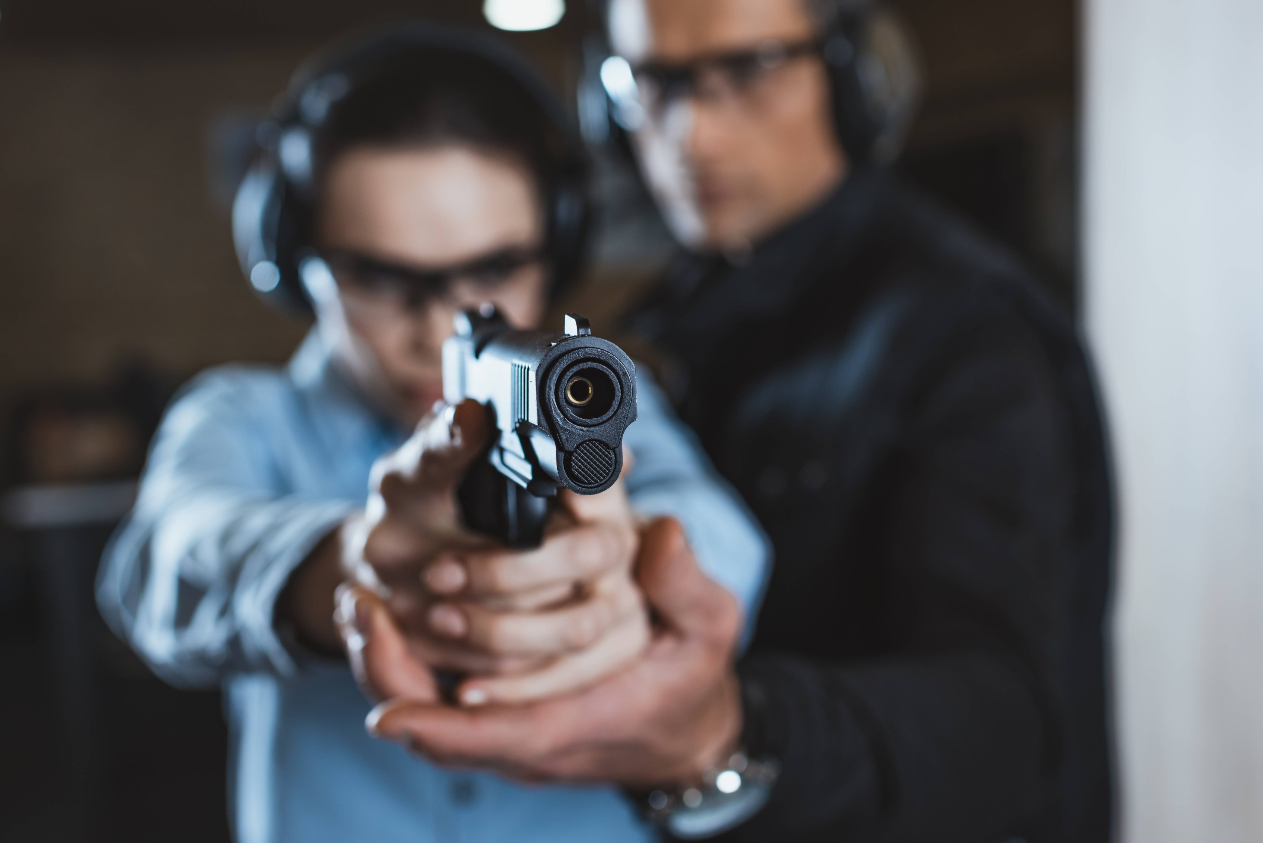 Instructor helping customer in shooting gallery with gun on foreground